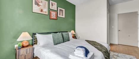 A bedroom with a bed, nightstands, a green wall, and framed pictures.