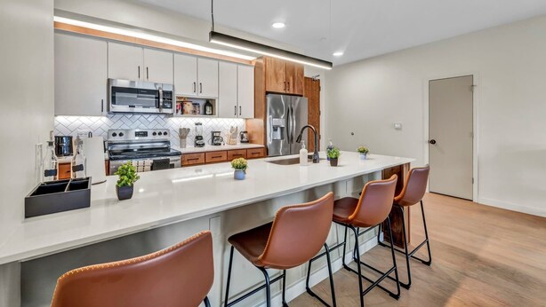 Cozinha moderna com ilha central, eletrodomésticos de aço inoxidável e área de bar com banquetas.