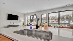 A modern kitchen with a large sink, a flat-screen TV mounted on the wall, and large windows offering a view of the outside. - Cleveland Clinic w KingBed,Balcony,Gym,Parking,WD (Cleveland)