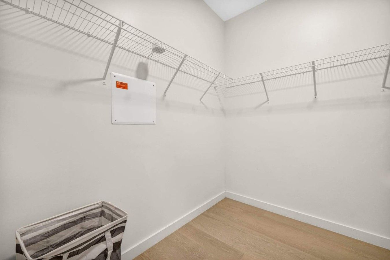 Une pièce avec un mur blanc, un plancher en bois et une étagère en métal.