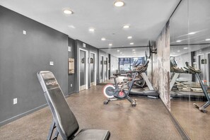 Een fitnessruimte met trainingsapparatuur, een spiegelwand en een interieur in grijstinten.