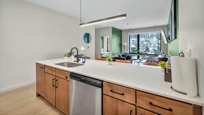A modern kitchen with a dishwasher, wooden cabinets, and a large island. - Little Italy & CWRU w King BedGymParkingWD (Cleveland)