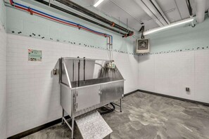 Un baño moderno de estilo industrial, con un lavamanos de acero inoxidable, paredes de azulejos blancos y fontanería a la vista.
