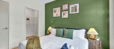 Un dormitorio con una cama, paredes verdes y cuadros enmarcados.