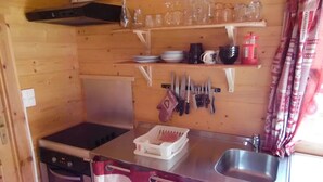 Eine kompakte Küche mit Herd, Spüle und Utensilienhalter. Über der Arbeitsplatte befinden sich Regale mit Gläsern und Tellern.