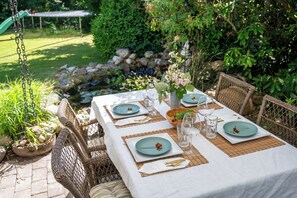An outdoor dining table set with plates, cutlery, and glasses, surrounded by wicker chairs and a white tablecloth. - Quiet forest home, few steps from LEGOLAND®, Lalandia & LEGO - calm & cozy (Billund)