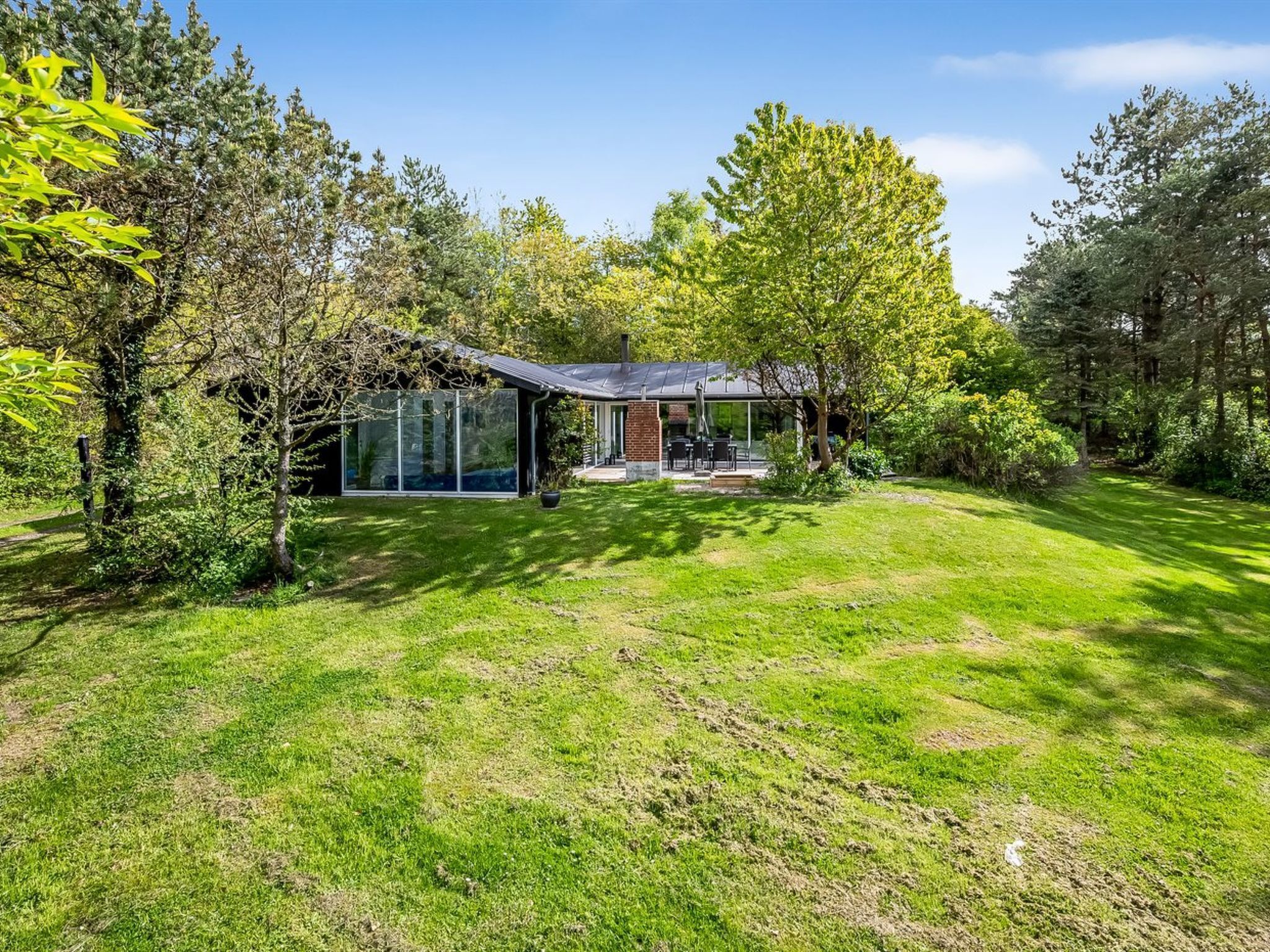 A modern house with a glass conservatory, a patio with outdoor furniture, and a well-maintained lawn.