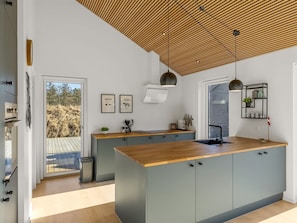 Eine moderne Küche mit einer Holztheke, Pendelleuchten und Blick ins Freie.