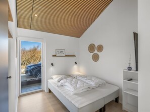 Ein modernes Schlafzimmer mit einem Bett, einer zur Außenseite führenden Tür und Blick auf ein Auto durch die Tür hindurch.