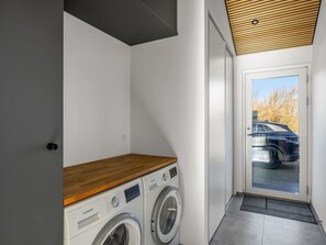 Ein Waschraum mit zwei weißen Waschmaschinen, einer Holzauskładung und einer Glastür, die nach draußen führt.