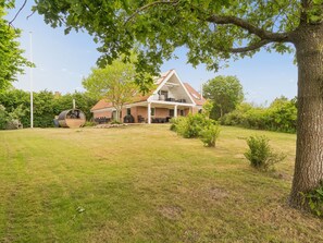 Una casa con un jardín amplio, una zona de barbacoa y un árbol en primer plano.