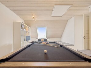 Una mesa de billar con una bola blanca, una estantería y una ventana en una habitación con techo y paredes de madera.