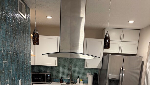 Een moderne keuken met een groot eiland, roestvrijstalen apparatuur en een spatwand met turquoise tegels.