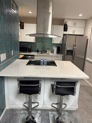 Una cocina moderna con una isla grande, electrodomésticos de acero inoxidable y salpicadero con baldosas color turquesa.