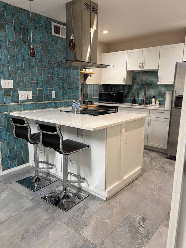 Una cocina moderna con una isla central, taburetes de bar, un microondas y un refrigerador de acero inoxidable.