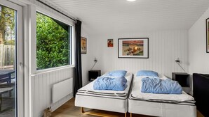 Ett rum med två sängar, ett fönster med utsikt över grönområden, en affisch på väggen och ett bord utanför.