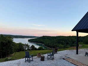 Blick auf einen See mit Stühlen und Feuerstelle, umgeben von einer Laube.