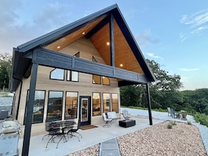 A modern house with a large patio, outdoor seating, and a view of the surrounding landscape. - Brand-New Beaver Lake Cabin - Lake Views - Fire Pit - Sleeps Up To 9 (Garfield)