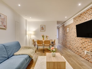 A modern living room with a blue sofa, a dining table with chairs, a TV mounted on a brick wall, and a small wooden coffee table. - Atelier Parisien - 4P - Montparnasse Station (Paris)