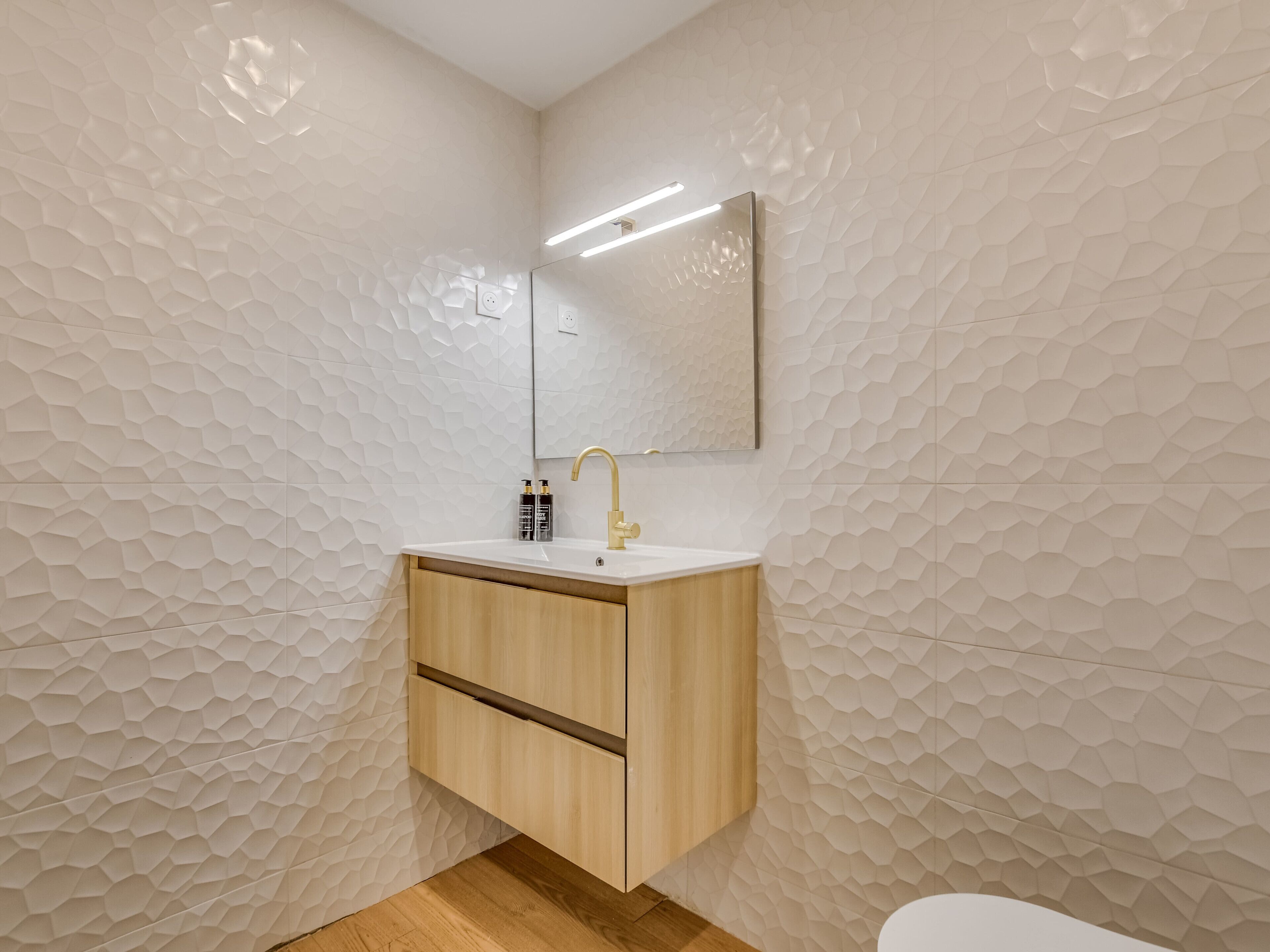 A bathroom with a geometric patterned wall, a wooden cabinet with a sink, and a mirror above the sink.
