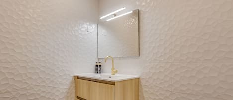 A bathroom with a geometric patterned wall, a wooden cabinet with a sink, and a mirror above the sink.