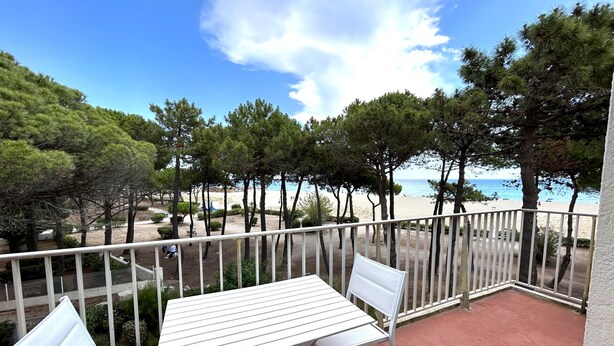 Ein Balkon mit Tisch und Stühlen, der Blick auf einen Strand mit Bäumen und einem klaren Himmel freigibt.