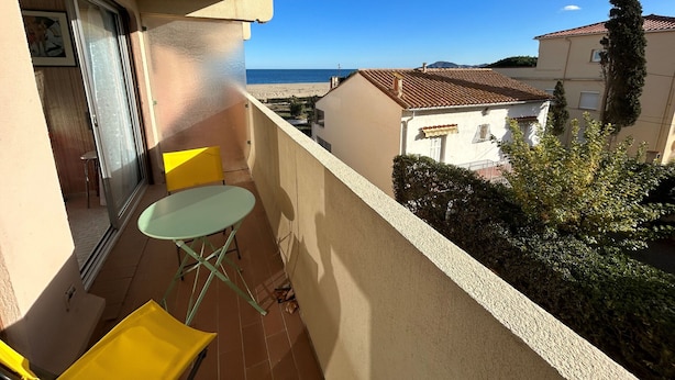 Ein Balkon mit Tisch und Stühlen, der Blick auf einen Strand und umliegende Gebäude bietet.