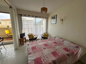 A bedroom with a bed, two chairs, a TV, and a window with curtains. - Studio with balcony and parking by the beach (Argelès-sur-Mer)