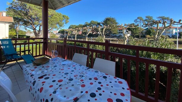 An outdoor patio with a table set for dining, surrounded by a red railing and trees. - T3 Duplex near Capbreton port with parking, 5 pers. (Capbreton)