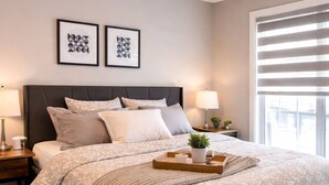 Un dormitorio con cama, mesitas de noche, una ventana con persianas y dos cuadros en la pared.