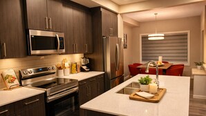 Una cocina moderna con armarios de madera oscura, electrodomésticos de acero inoxidable, una isla central con un fregadero y un comedor con sillas rojas.