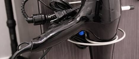 A hair dryer mounted on a wall with a cord and a plug.