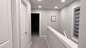 Un pasillo con puertas blancas, una ventana con persianas y luces empotradas en el techo.