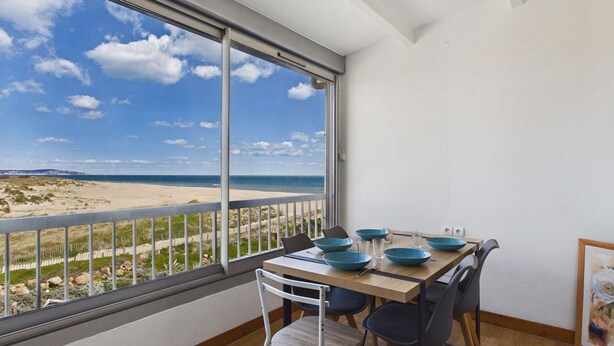 Un coin repas avec une table et des chaises, de grandes fenêtres donnant sur la plage et un tableau encadré au mur.