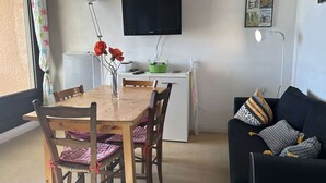 Een kleine woonruimte met een eettafel, stoelen, een bank, een televisie en een klein keukentje.
