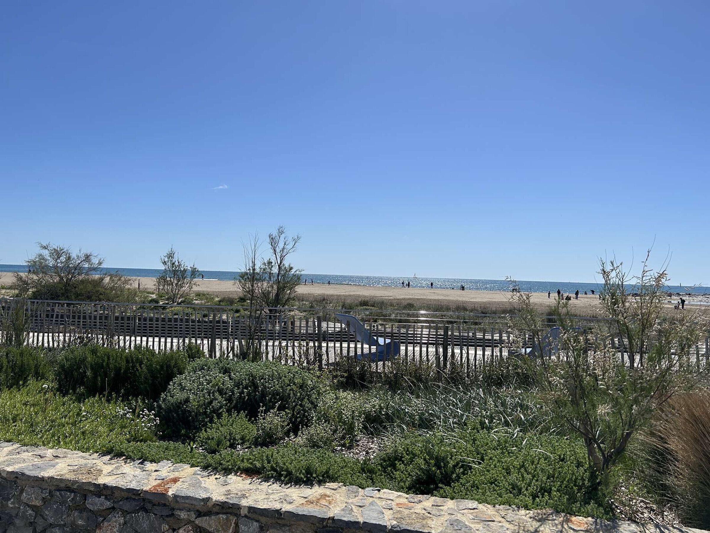 Vista costera con muro de piedra, vegetación y cielo despejado.