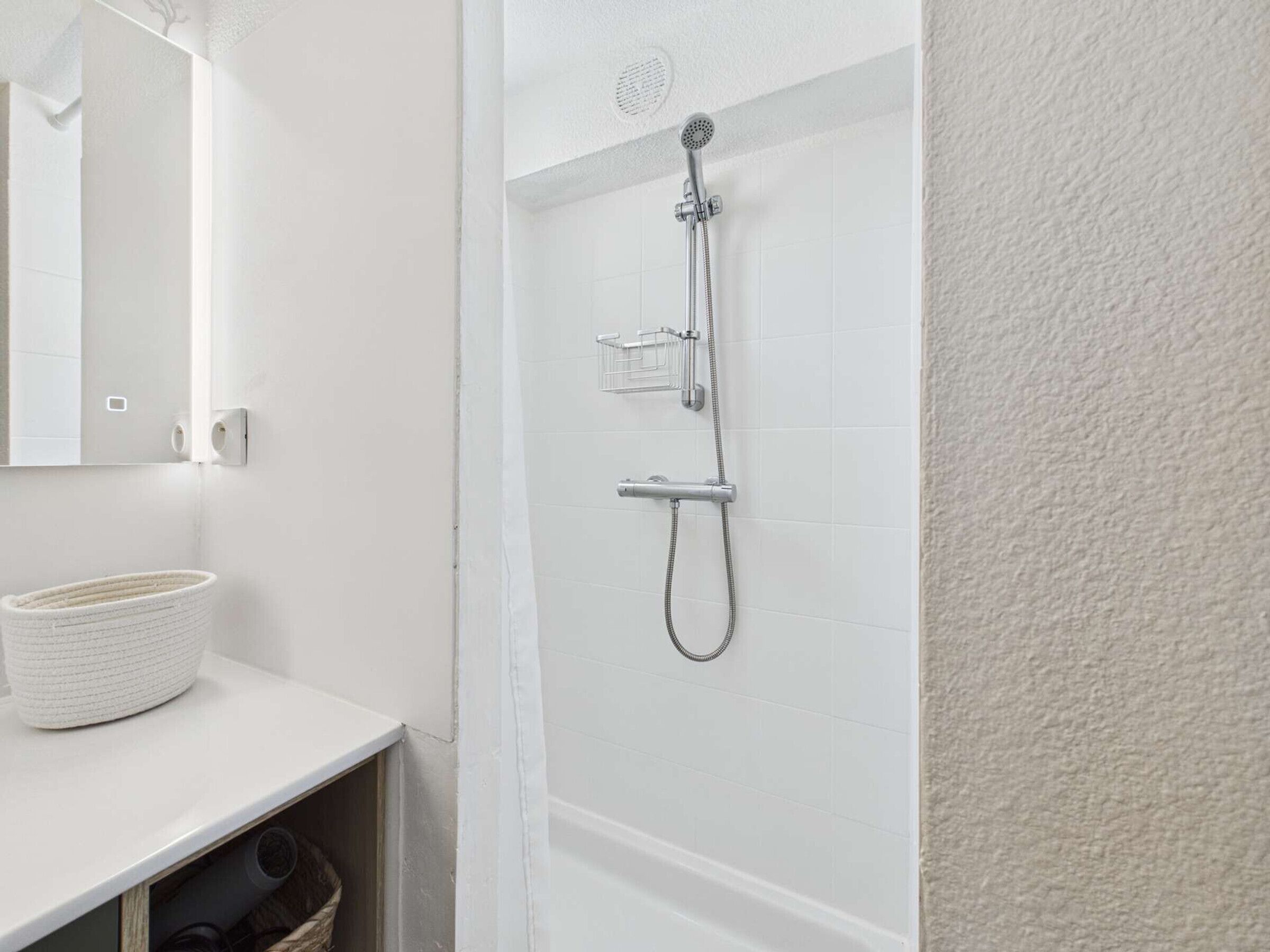 A bathroom with a white sink, a mirror, a shower with a handheld showerhead, and a towel rack.