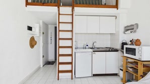 Cozinha compacta com armários brancos, micro-ondas e escada de madeira.