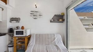 Um quarto pequeno e compacto com uma cama, micro-ondas, uma estante de livros e uma janela.