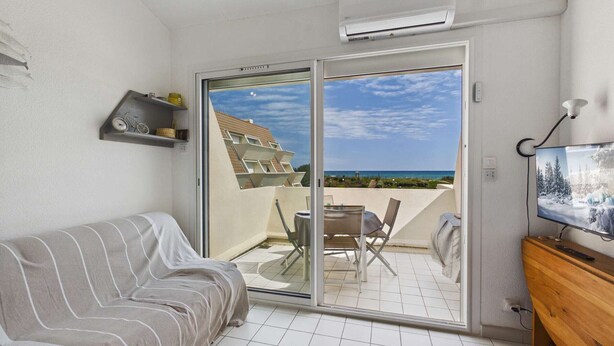 Varanda com vista para o mar, um sofá, uma televisão e uma mesa com cadeiras.