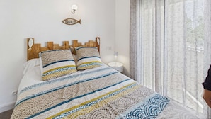 Uma cama com colcha listrada, cabeceira de madeira e luminária em formato de peixe fixada na parede.
