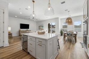 A modern kitchen with a central island, pendant lighting, and a dining area with a table and chairs. - Grateful Getaway | Private Pool/Spa | 6-Seater Golf Cart | Arcade Games (Miramar Beach)