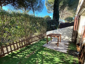 Eine Terrasse mit Holztisch und Stuhl, umgeben von einer Hecke und einem Holzzaun.