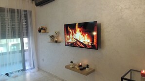 Een woonkamer met een open haard, een tv aan de muur en een glazen tafel.