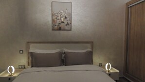 Een slaapkamer met een bed, twee nachtkastjes met lampen, een houten garderobe en een stadsgezichtschilderij aan de muur.