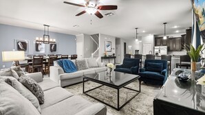Ein modernes Wohnzimmer mit einer Couch, Sesseln, einem Couchtisch und einem Essbereich mit Stühlen und einer Chandeliebre.