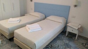 A hotel room with two beds, each with a white mattress and pillows, a small bedside table with a lamp, and a patterned floor. - La Locanda b&b Dandana (Orgosolo)
