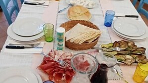 A dining table set for a meal with plates, cutlery, glasses, and various food items. - La Locanda b&b Dandana (Orgosolo)