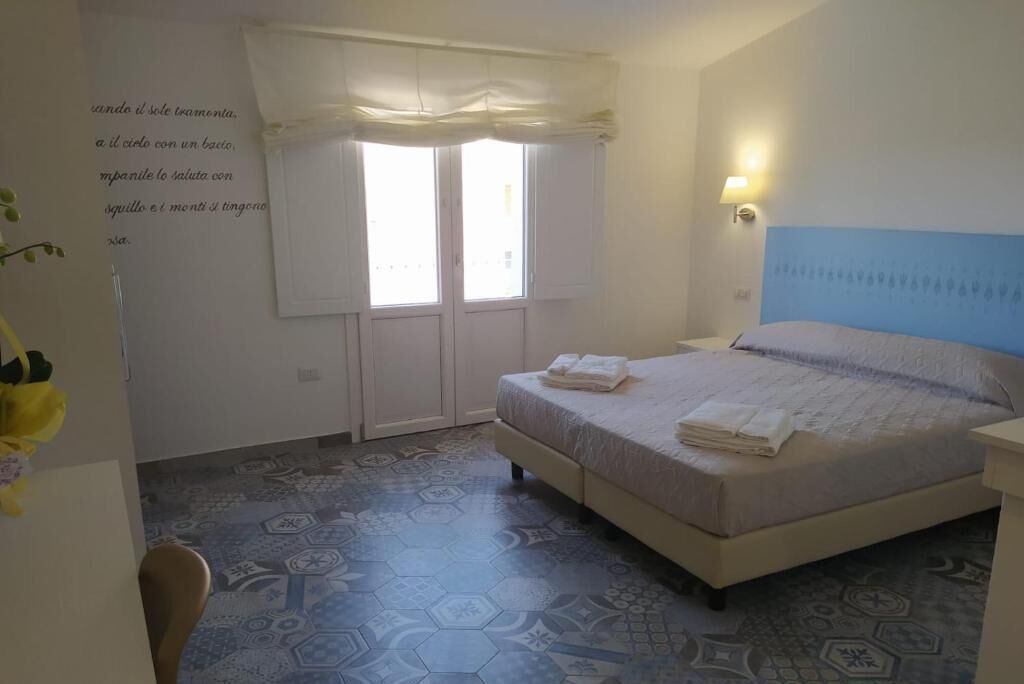 Una camera da letto con un letto, una finestra con tende, un muro con una citazione e un pavimento decorato.