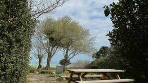 Une table de pique-nique et un banc sont installés dans un espace naturel, au milieu des arbres, avec vue sur la mer.
